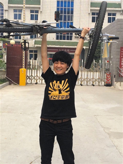 法院门前,马户把一辆自行车举过头顶,以证明她可以胜任快递员的工作。