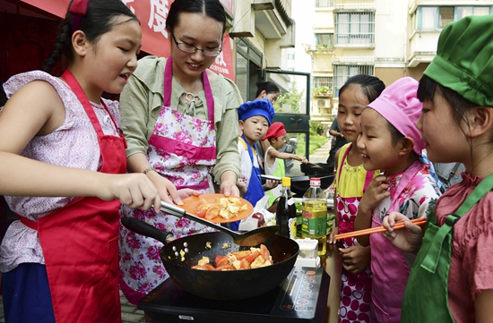 8月6日，志愿者（左二）指导小朋友炒菜。